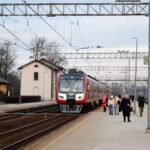 Пассажирский поезд на железнодорожной станции рядом с платформой и пассажирами.