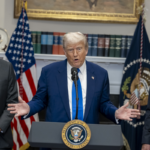 Дональд Трамп выступает у трибуны в официальном помещении, рядом стоят два мужчины в костюмах.