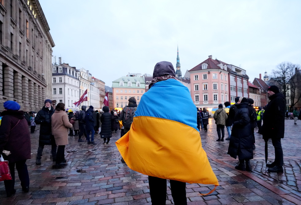 Человек, укрывшийся флагом Украины, стоит на площади среди людей в городе.