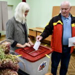Два человека голосуют на избирательном участке, опуская бюллетени в урну.