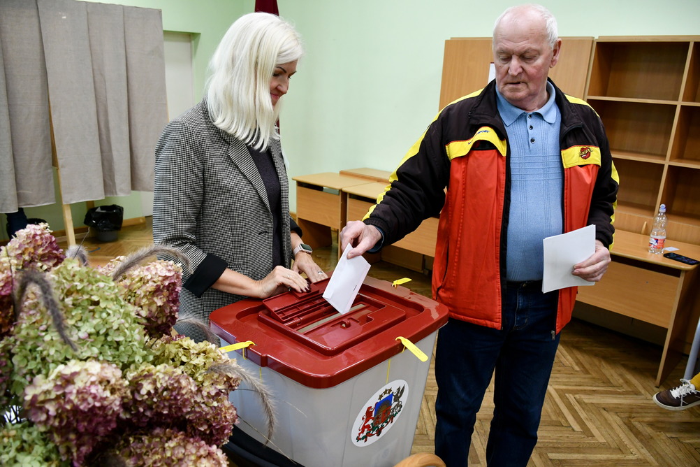Два человека голосуют на избирательном участке, опуская бюллетени в урну.