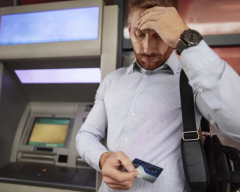 Мужчина у банкомата держит банковскую карту и выглядит обеспокоенным.