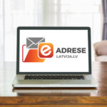 Ноутбук на столе с логотипом e-adrese Latvija.lv на экране.