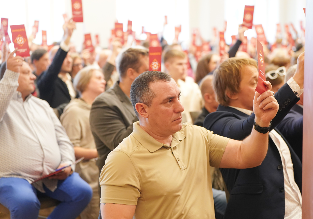 Мужчина на политическом собрании поднимает красную карточку для голосования.
