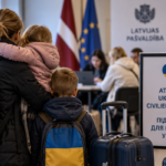 Украинская семья с детьми и багажом у стойки помощи в здании с латвийской и европейской символикой.