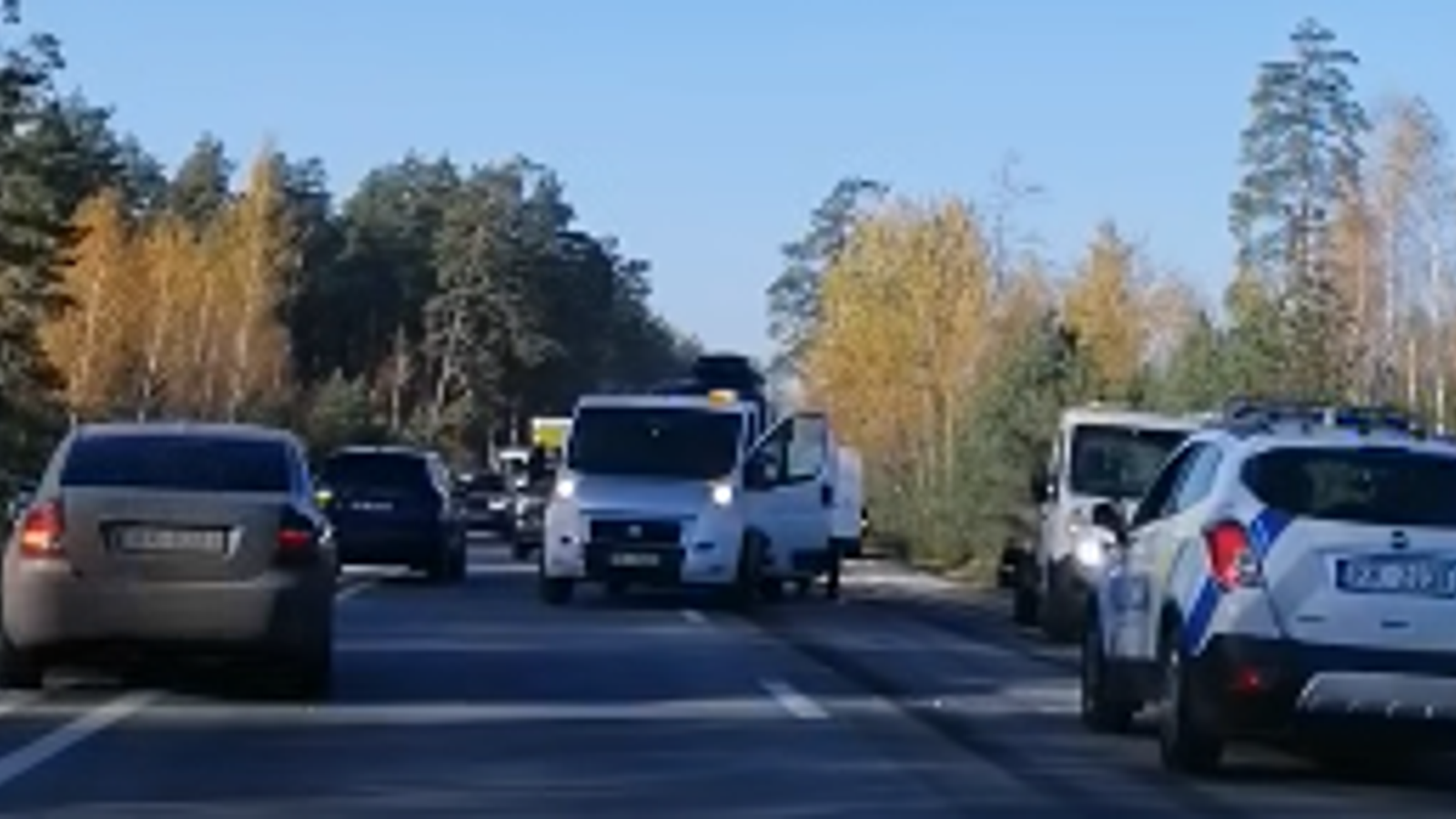Несколько автомобилей стоят в пробке на загородной трассе среди деревьев.
