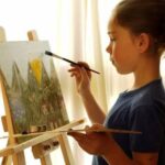 Девочка рисует на холсте у мольберта.