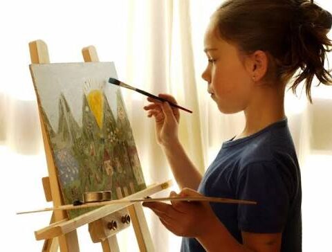 Девочка рисует на холсте у мольберта.