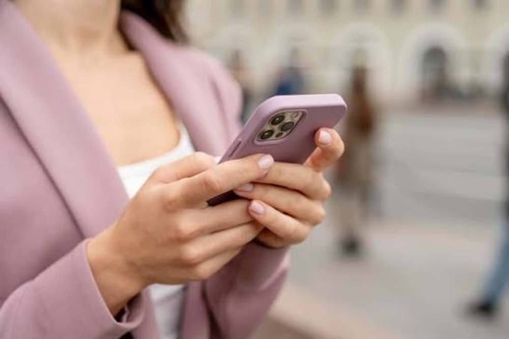 Женщина держит смартфон в руках на улице.