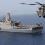 Военный корабль в море, над ним летит вертолёт.
