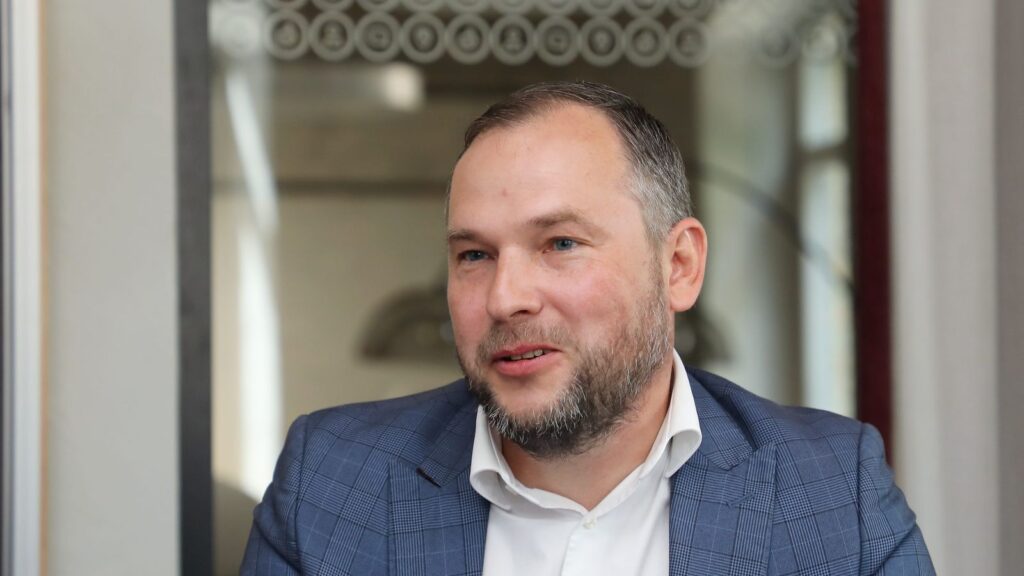 Портрет мужчины в синем клетчатом пиджаке и белой рубашке в помещении.