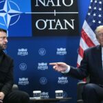 Владимир Зеленский и Дональд Трамп сидят на встрече на фоне логотипа НАТО и флагов США и Украины.