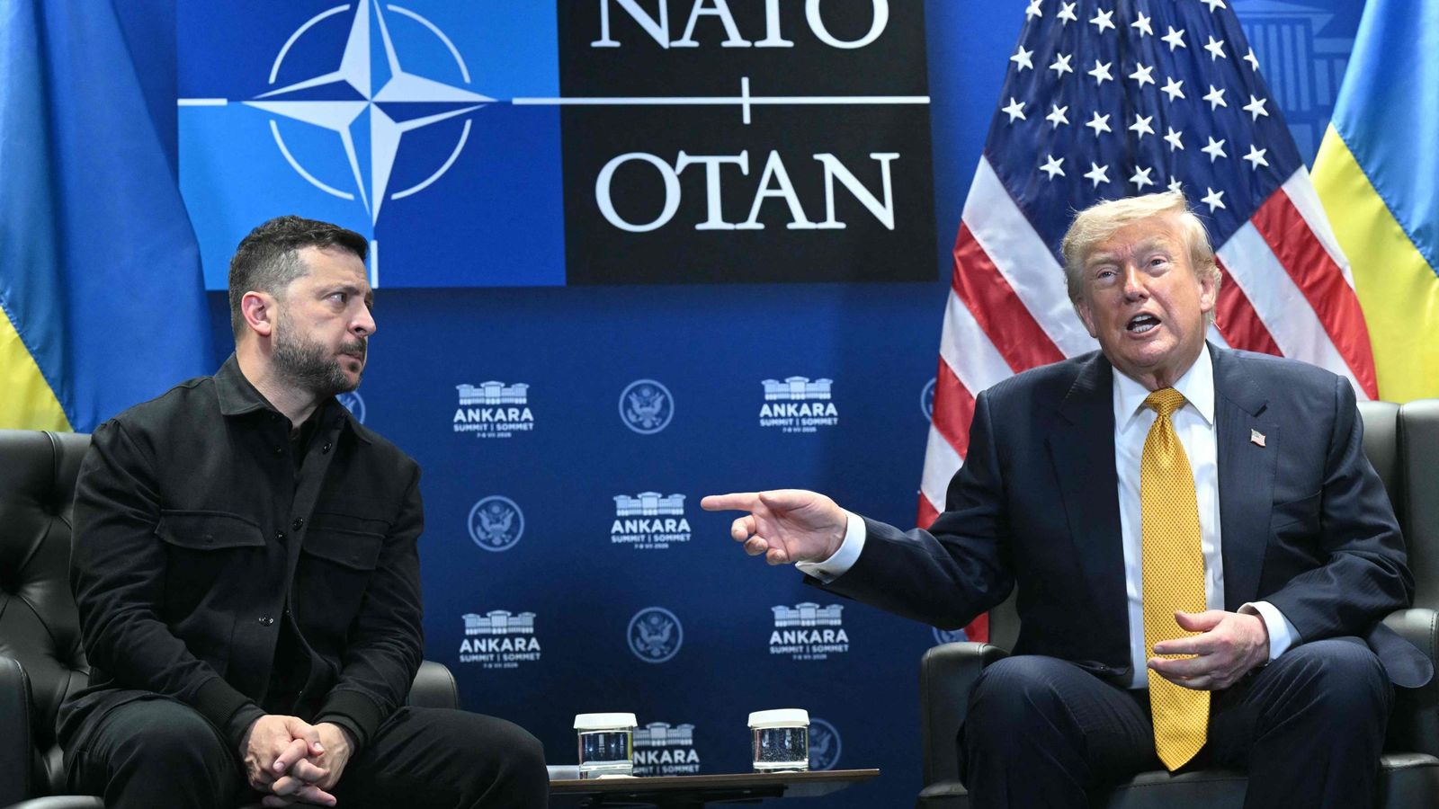 Владимир Зеленский и Дональд Трамп сидят на встрече на фоне логотипа НАТО и флагов США и Украины.