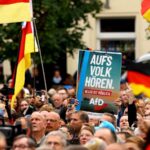 Crowd at a protest in Germany holding German flags and an AfD sign.