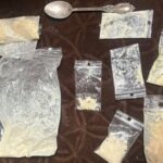 На тёмной поверхности разложены несколько пакетиков с порошкообразным веществом и ложка.