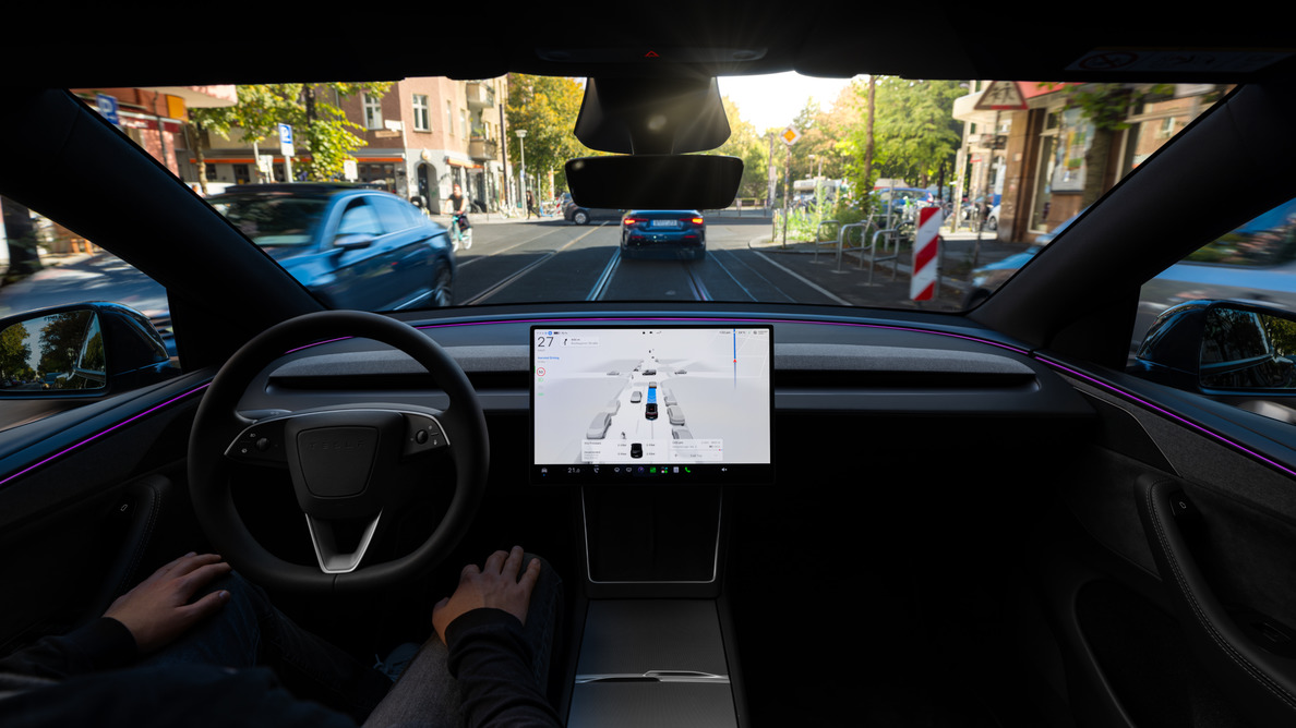 Интерьер Tesla с включенным экраном системы помощи водителю на дороге в городе.