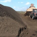 Трактор на торфяном поле рядом с большой кучей торфа.