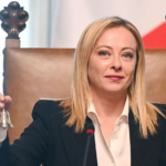 Женщина в деловом костюме сидит в кресле и держит маленький колокольчик.