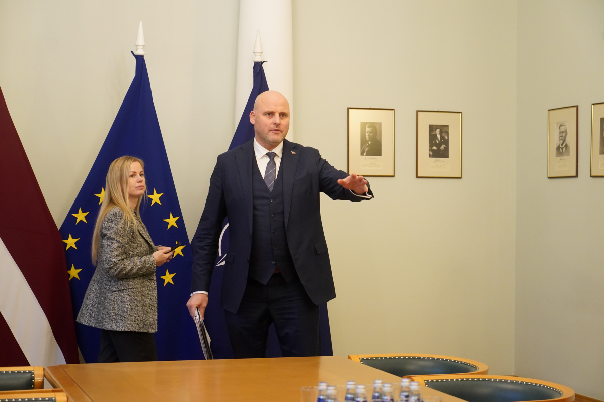 Премьер-министр Латвии Андрис Кулбергс в кабинете рядом с флагами Латвии и ЕС во время встречи.