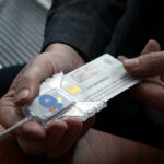 Руки держат пластиковую ID-карту с чипом, подключенную к считывателю.