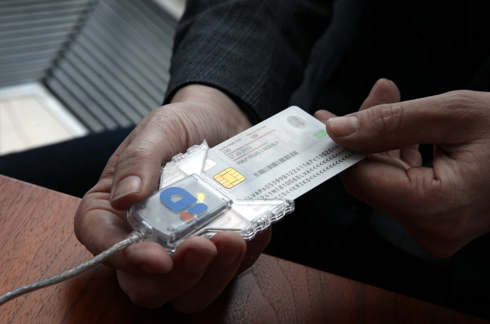 Руки держат пластиковую ID-карту с чипом, подключенную к считывателю.
