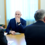 Андрис Кулбергс сидит за столом на встрече и слушает собеседников.