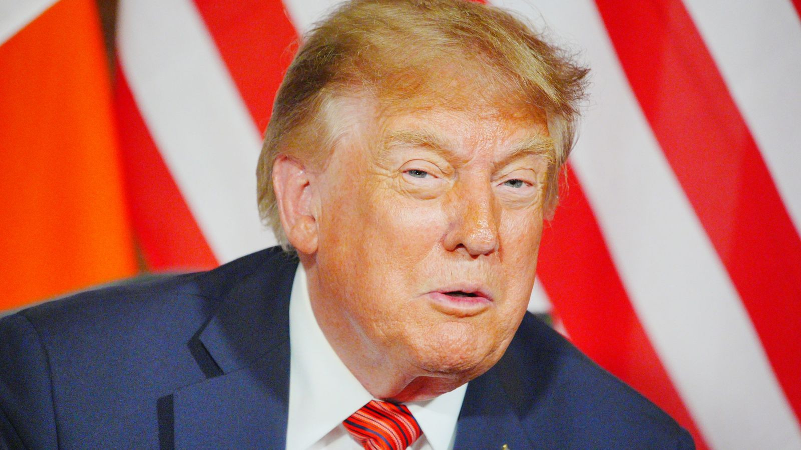 Дональд Трамп крупным планом на фоне красно-белых полос.
