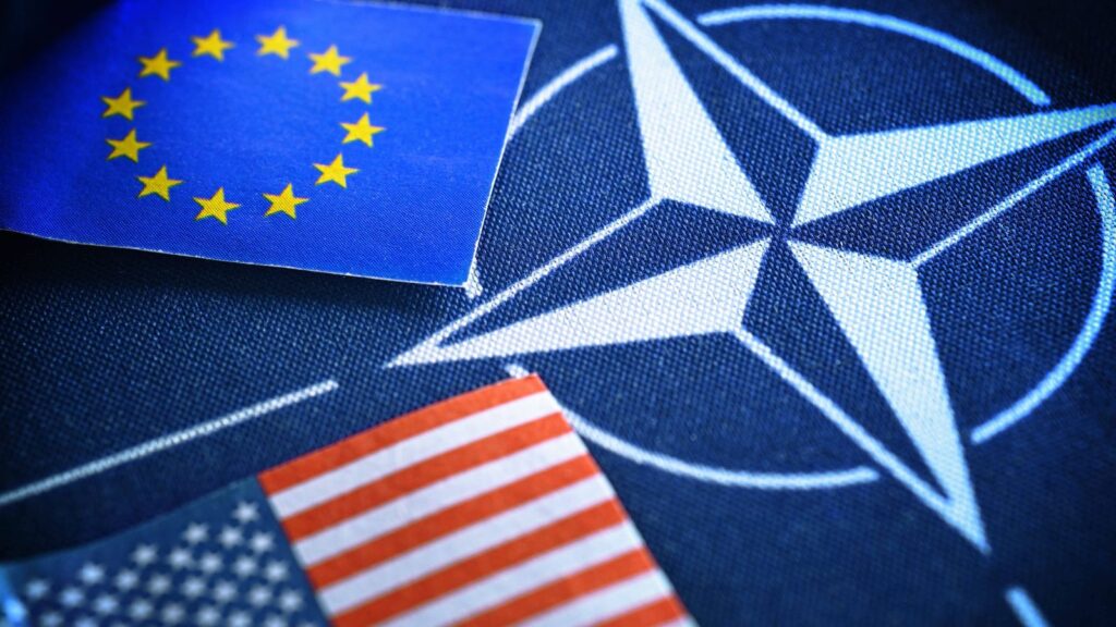 Значок НАТО на фоне флагов ЕС и США.