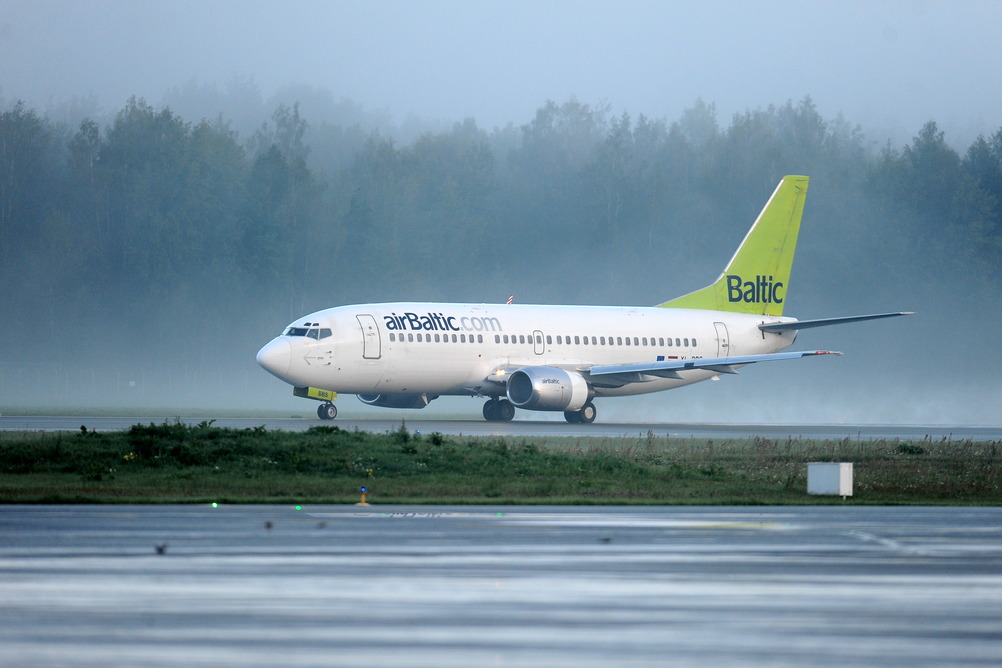 Самолет airBaltic на взлетно-посадочной полосе в дождливую погоду.