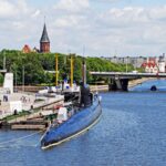 Подводная лодка у набережной на фоне центра Калининграда и моста через реку.