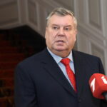 Янис Урбанович в костюме отвечает на вопросы журналистов у микрофонов.