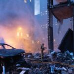 Пожарный тушит горящие обломки и поврежденное здание после взрыва в городе.
