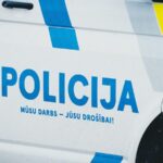 Боковая часть полицейской машины с надписью «POLICIJA» и сине-жёлтой маркировкой.
