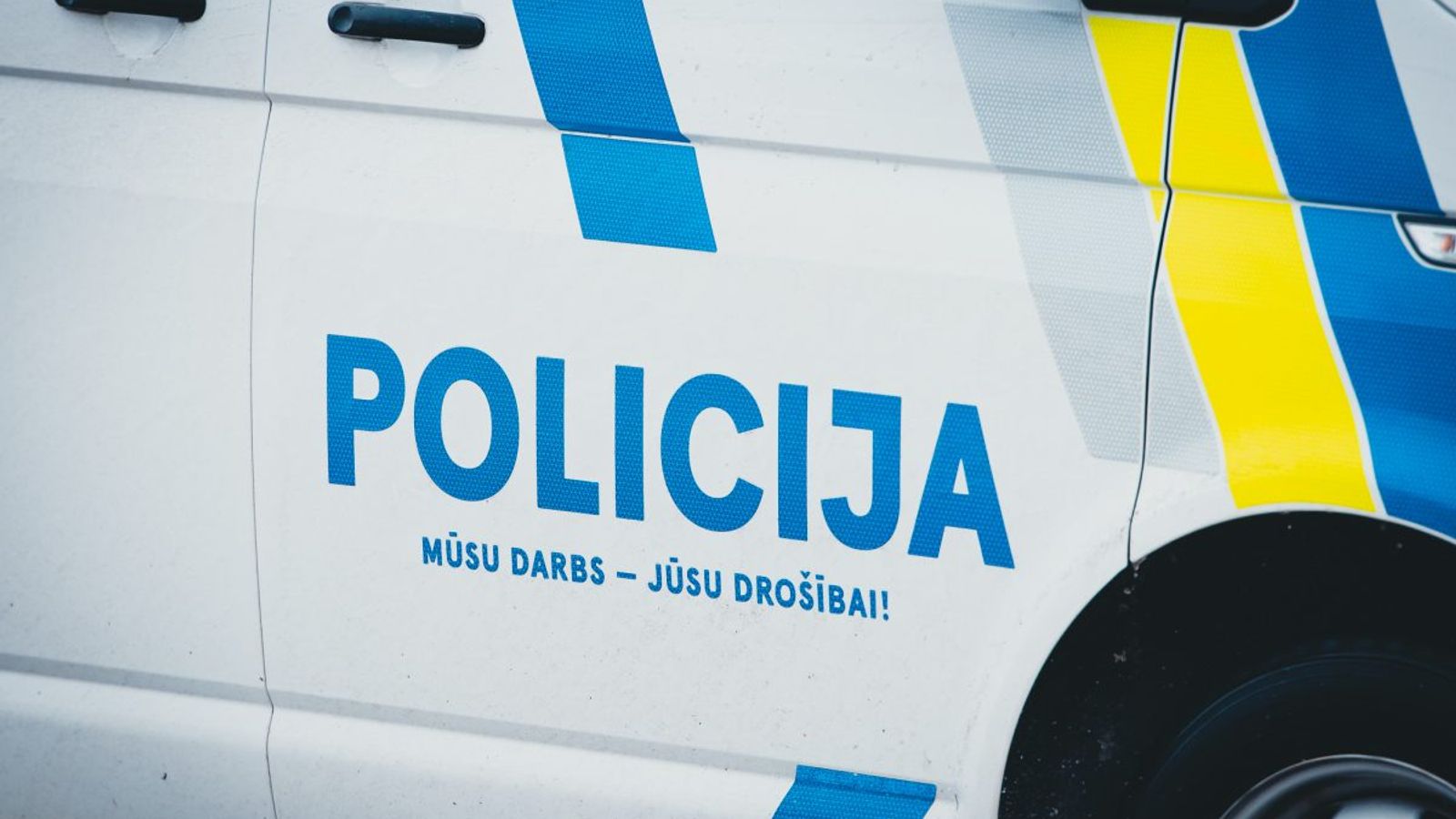 Боковая часть полицейской машины с надписью «POLICIJA» и сине-жёлтой маркировкой.