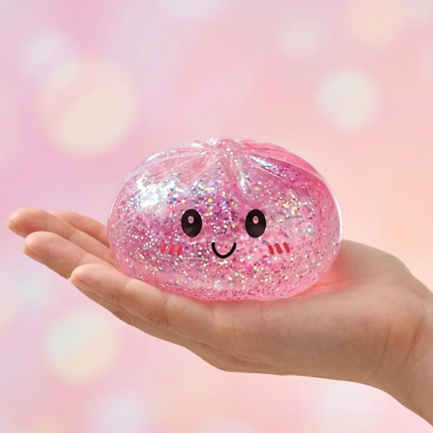 Рука держит розовую антистресс-игрушку Squishy Dumpling с блестками и нарисованным улыбающимся лицом.