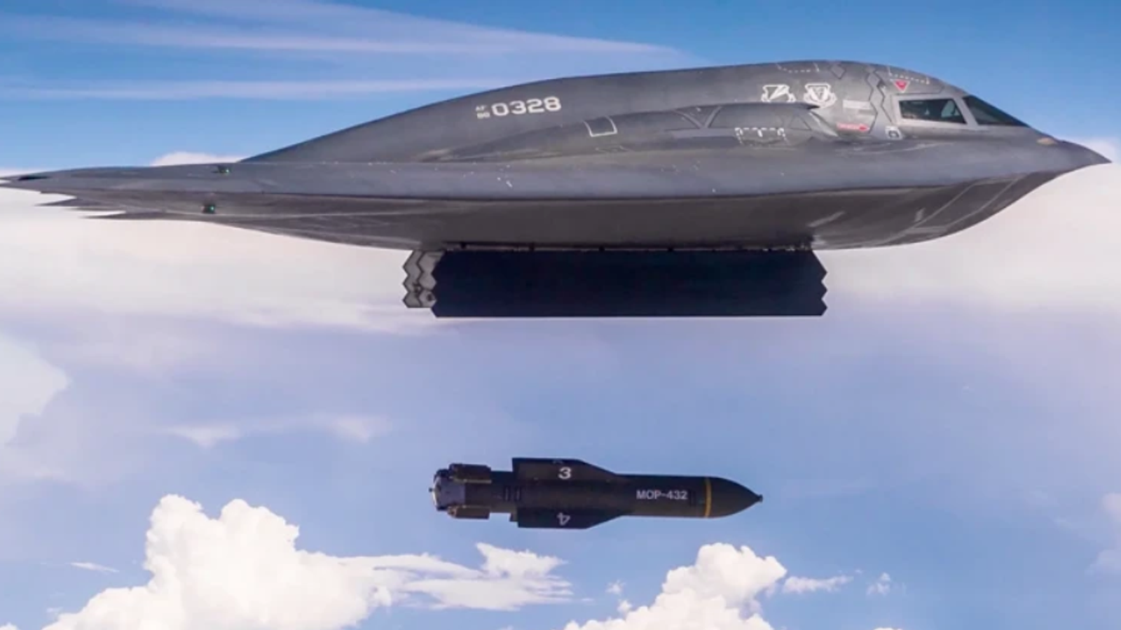 Бомбардировщик B-2 сбрасывает бомбу в полёте над облаками.