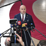 Андрис Кулбергс выступает перед журналистами у группы микрофонов в Брюсселе.