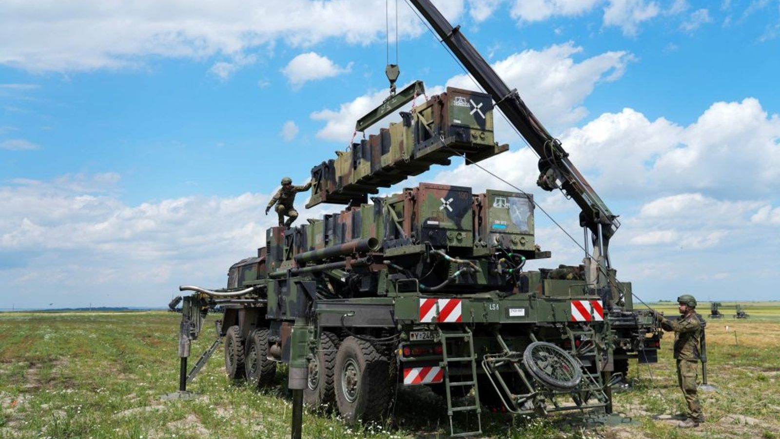 Военные рядом с установкой зенитного ракетного комплекса Patriot на открытой местности.